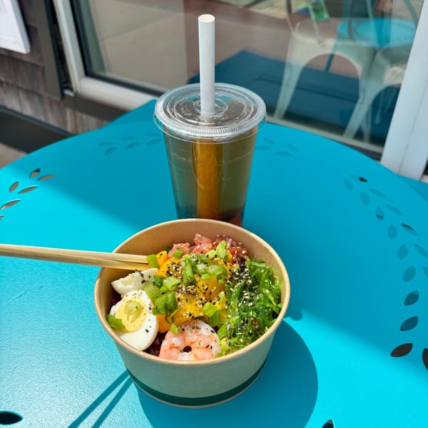 Gansett Poke bowl with shrimp, salmon, mango, seaweed, egg, and chopsticks, next to iced tea.